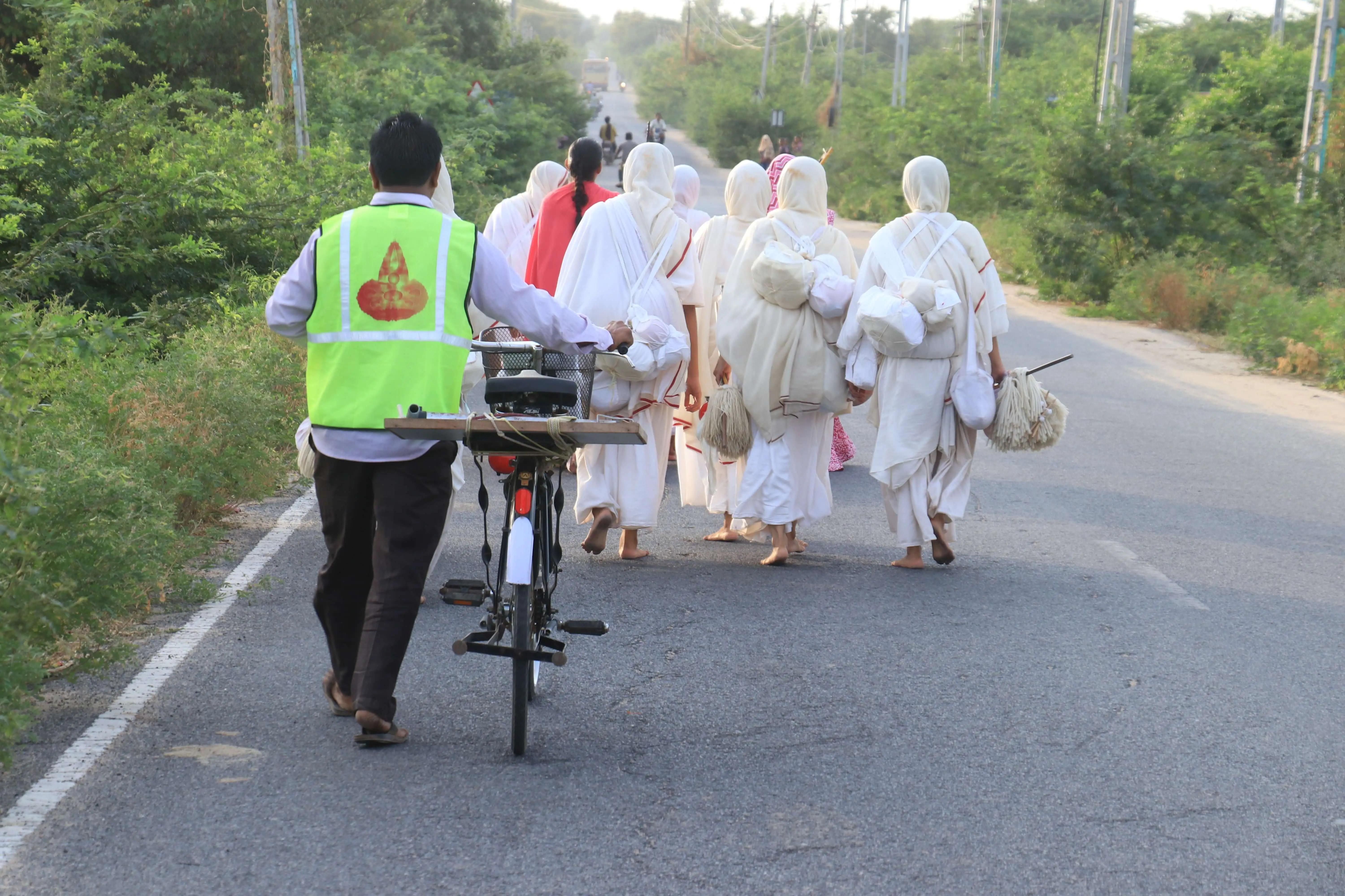 Group of people walking on a road with a person on a bicycle carrying supplies