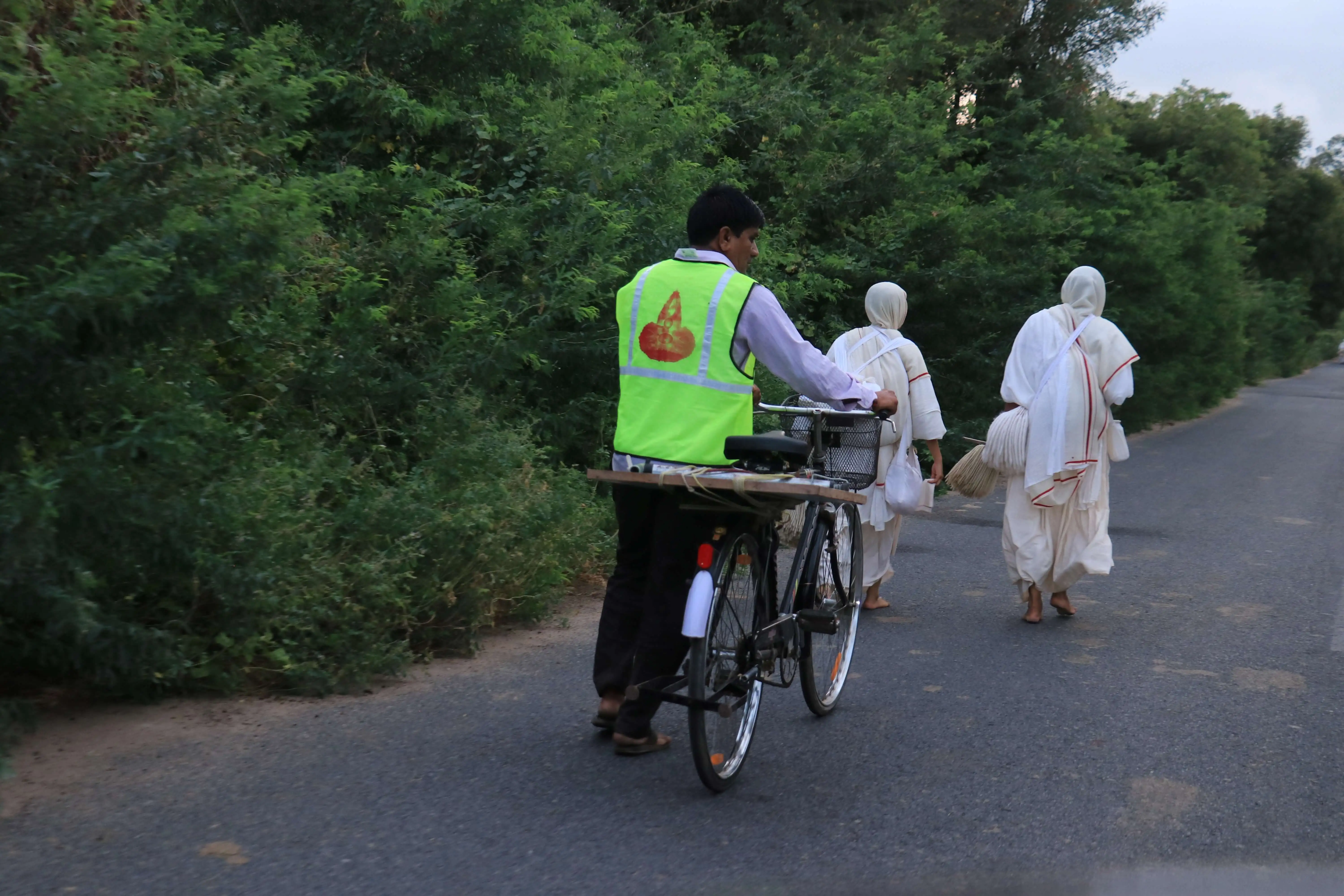 Person on a bicycle carrying supplies following a group of people walking on a road